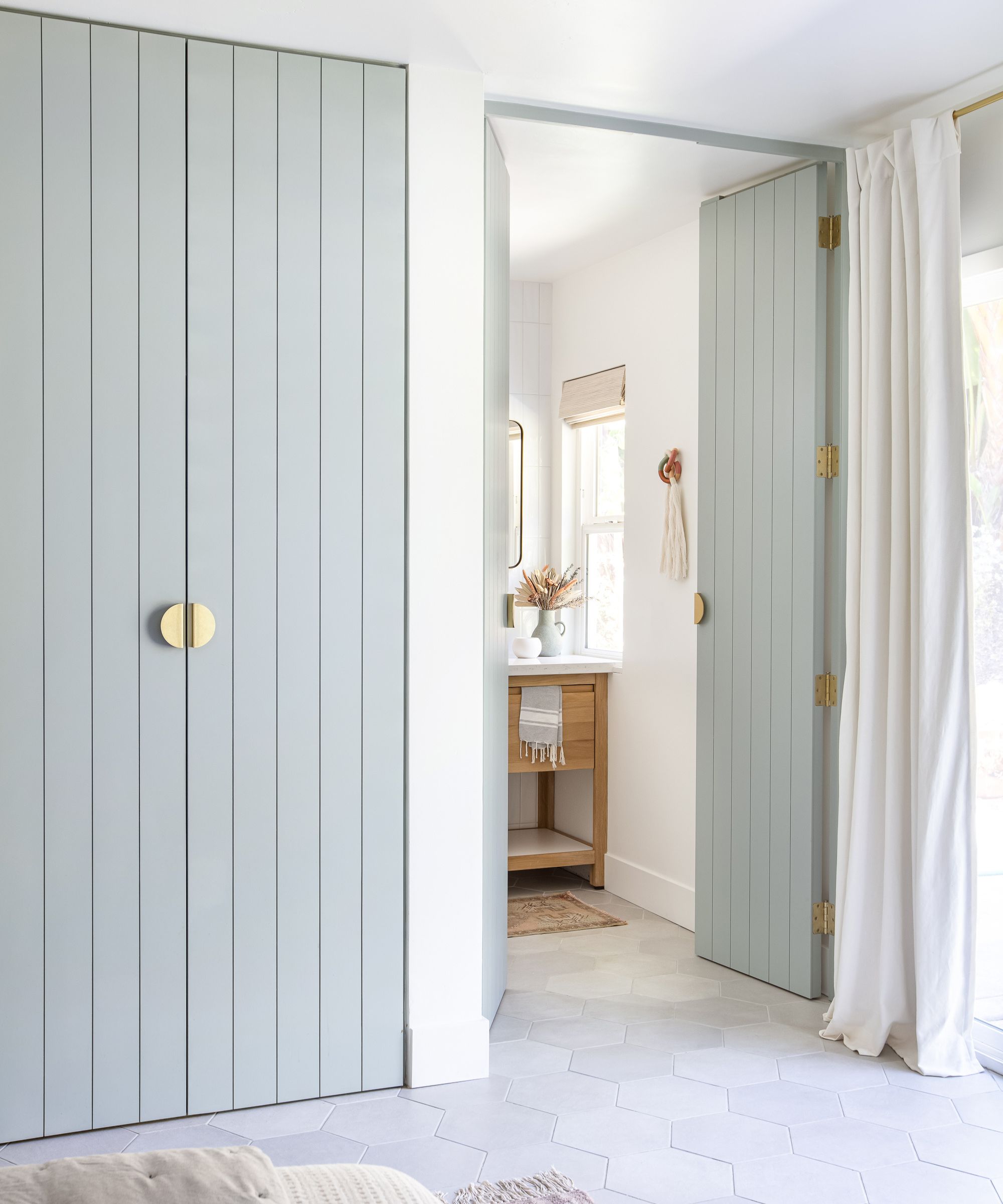 Bedroom with tiled floor, Oyster Bay by Sherwin-Williams painted cabinetry and door leading into a minimalist bathroom with a wooden vanity unit and white walls.