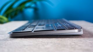 a black and grey budget wireless Bluetooth keyboard with a full-size layout and a numerical keypad is photographed against a blue background