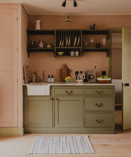 a tiny three cabinet size kitchenette in the cotswolds with green painted lower cupboards, a Thomas Crapper sink, and open shelving above