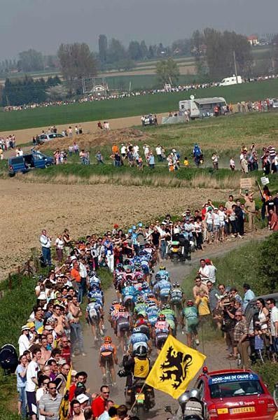The bunch kicks up dust on the cobbles