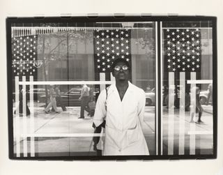 Black man in sunglasses leaning against glass façade reflecting stars and stripes and street scene