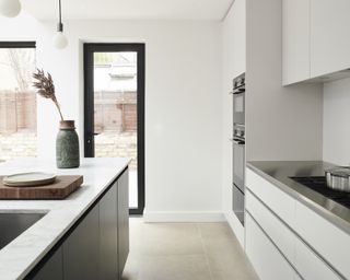 A modern kitchen with white handleless cabinets and grey island with quartzite worktop, and hob counter with stainless steel worktop