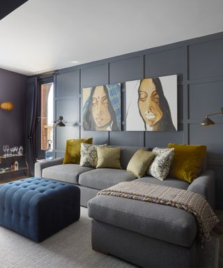 Dark grey living room ideas shown with mustard yellow accents in the cushions and artwork and a dark blue footstool.
