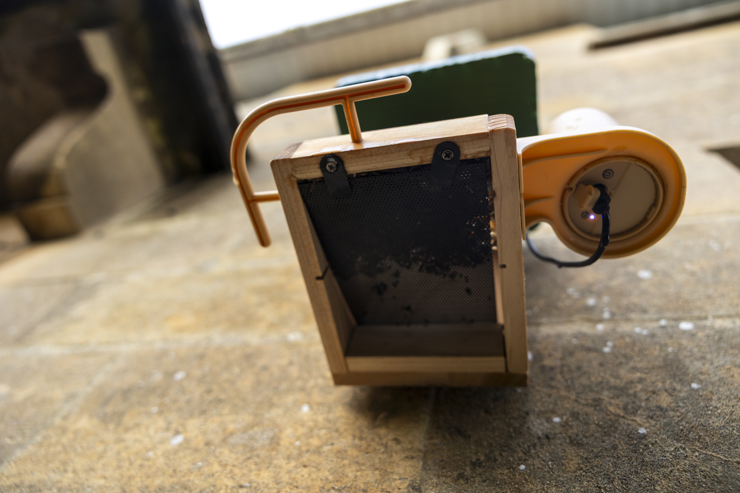 The underside view of the Birdfy Wood feeder on a stone wall