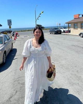 mid size fashion influencer Marina Torres walks on the streets of a beachside town wearing a romantic puff sleeve white dress