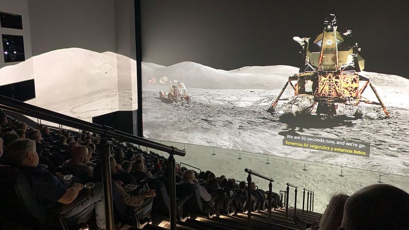 a panoramic photo of an Apollo lunar module on the moon is projected on a giant movie screen, as well as the theater&#039;s walls and floor