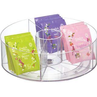 Clear acrylic turntable with dividers and square tea packets in pink, green, and purple colors.