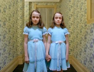 Two little girls in blue dresses stand in a wallpapered hallway in 'The Shining'