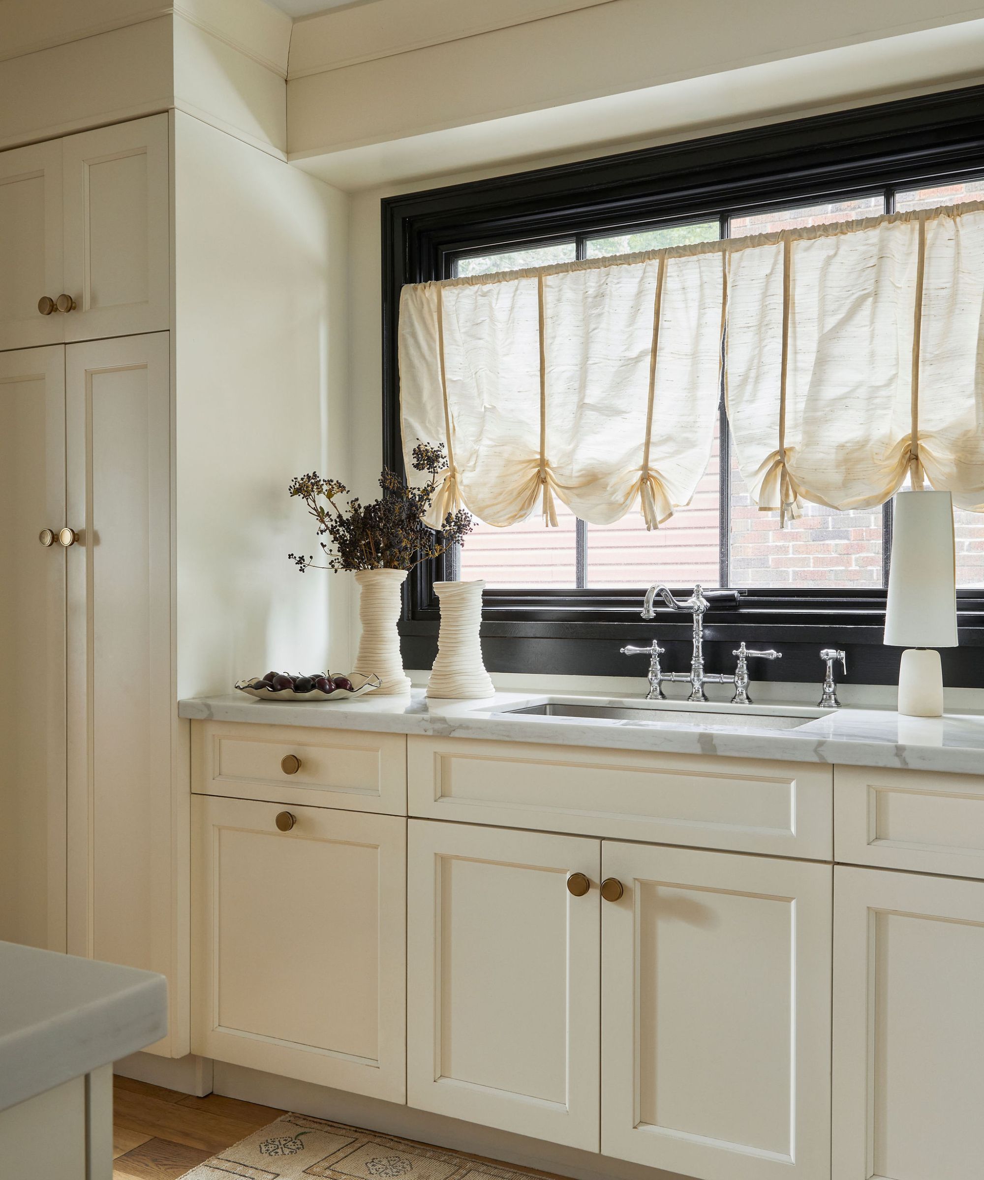 White kitchen with marble counterop and window above the sink with a white cafe curtain