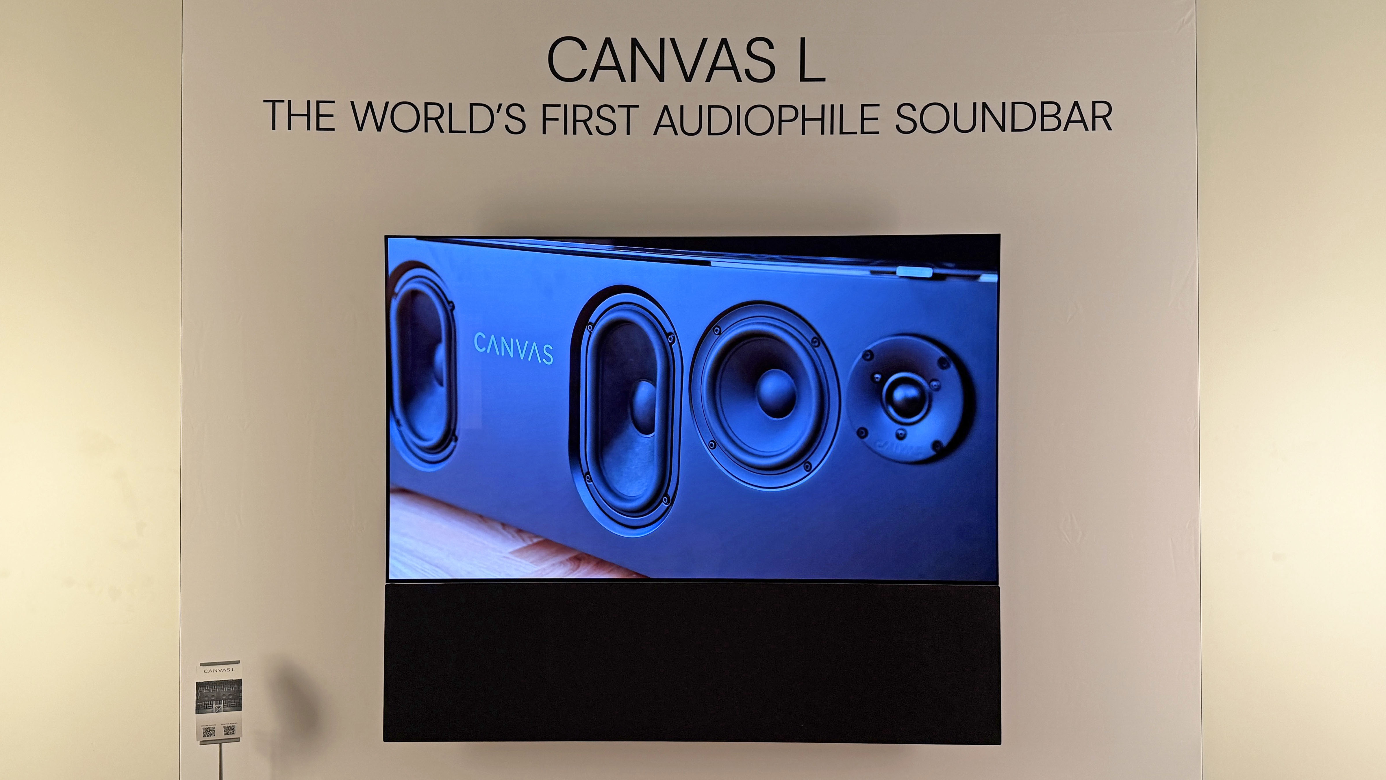 The Canvas L soundbar mounted under a TV on a wall in a showroom. The TV is showing an image of the speaker drivers in Canvas' previous soundbar