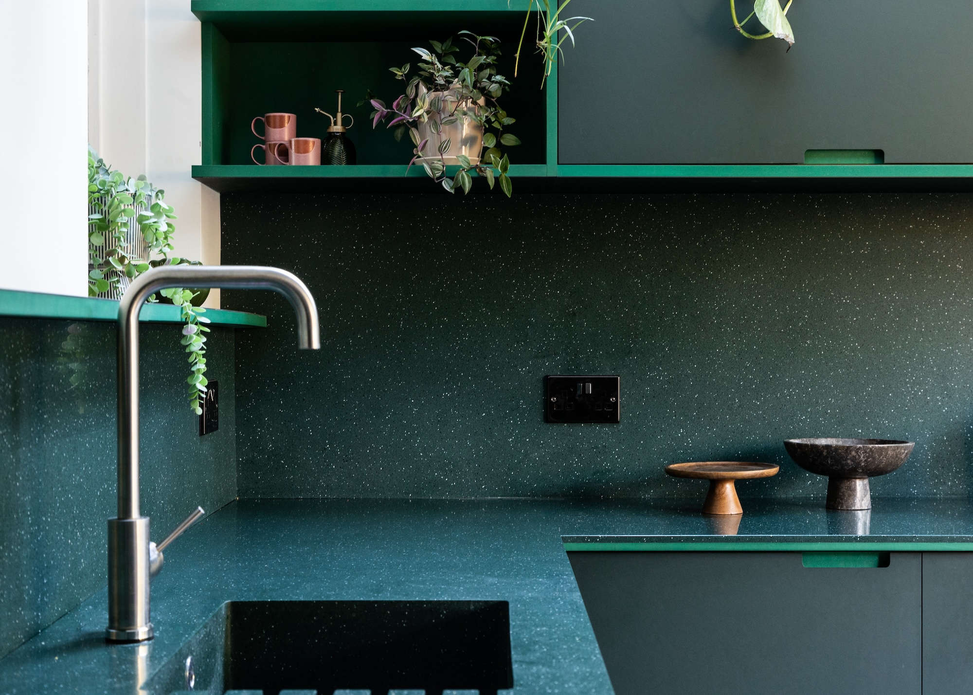 A deep blue kitchen with open shelving and a view of the sink as well as other kitchen accessories on top