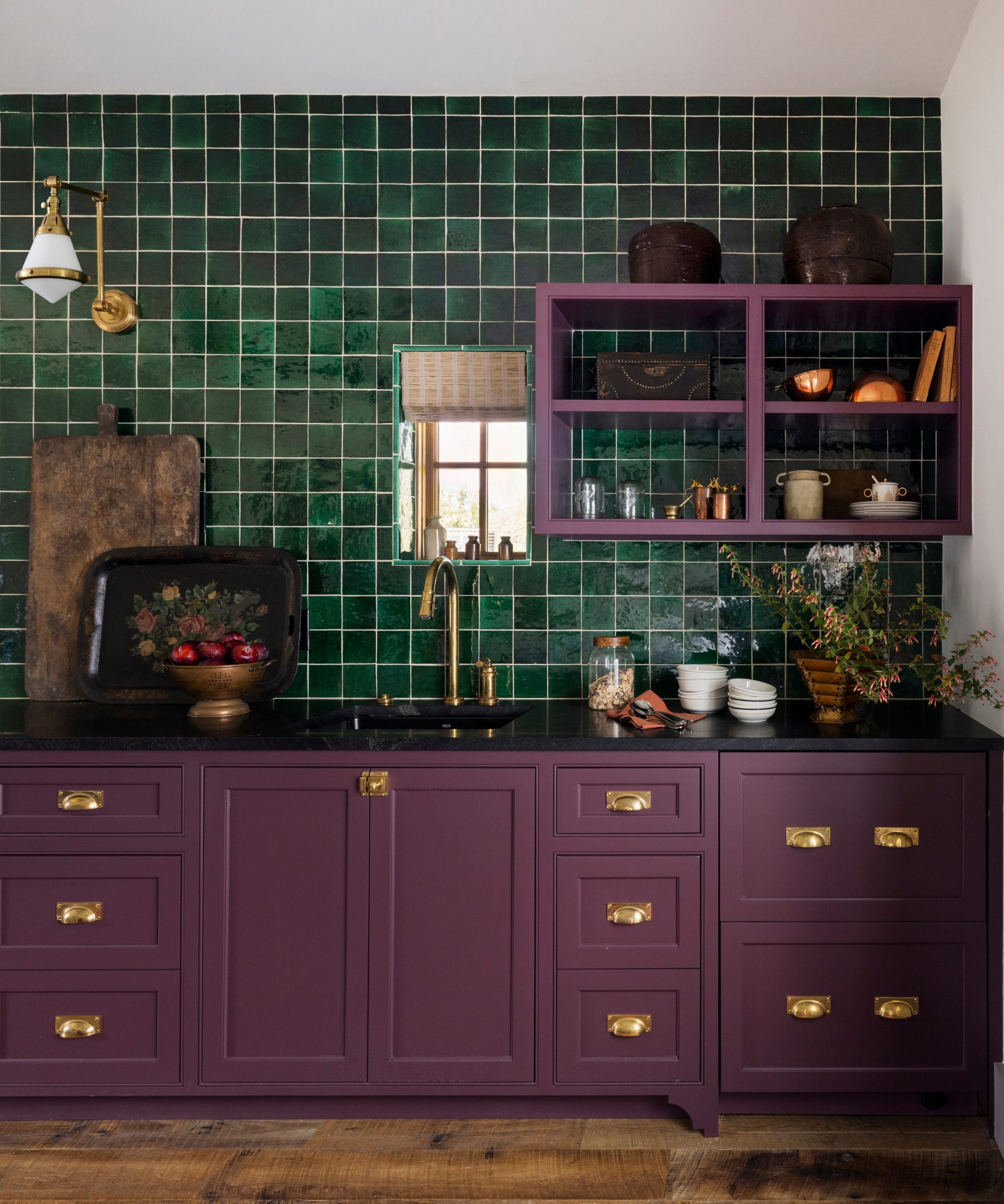 a rich purple kitchen with a emerald green tiles wall and brass hardware