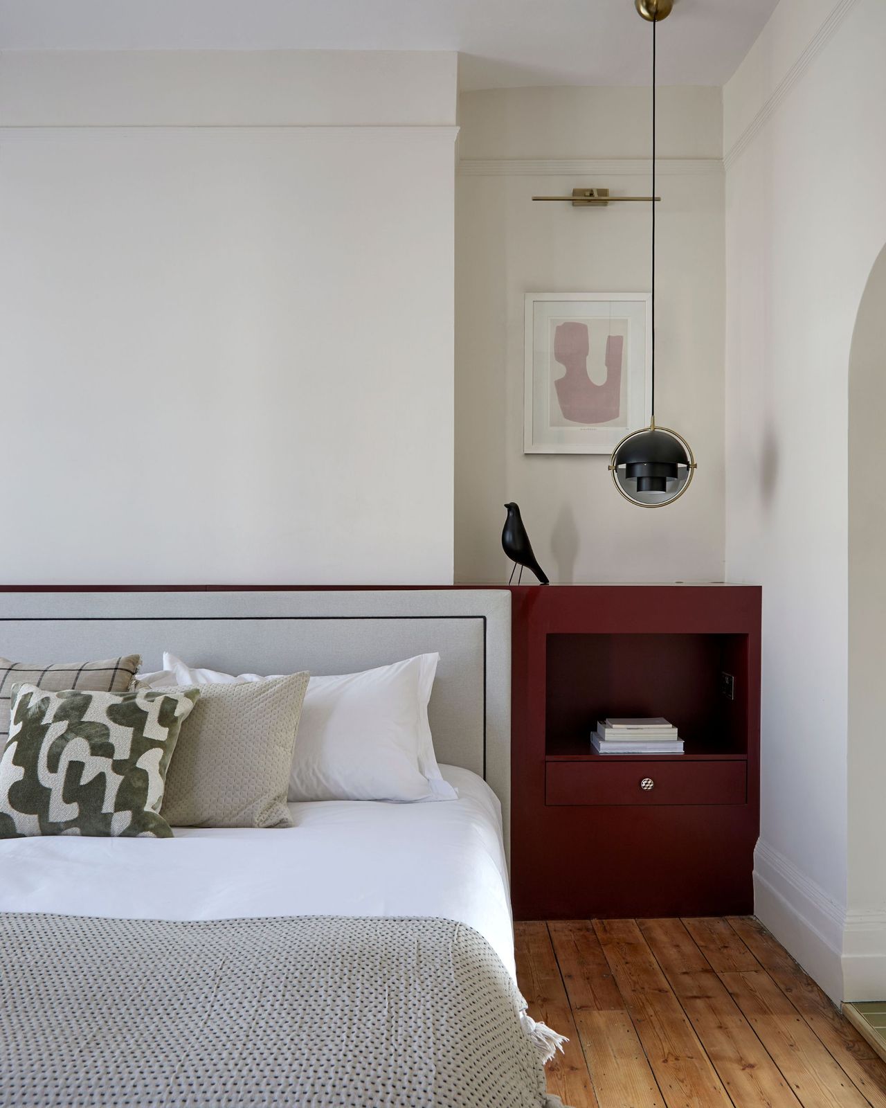 A modern neutral bedroom with built in nightstands and pendant ceiling bedside lamps with a headboard and lots of cushions on the bed