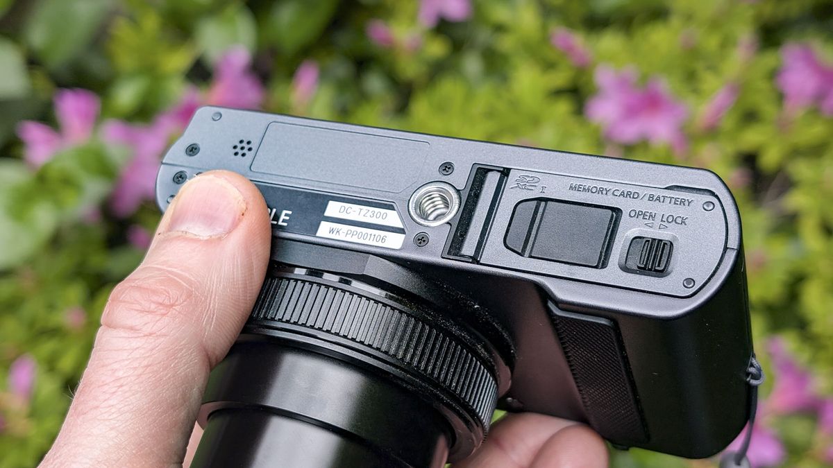 Close up of the Panasonic Lumix TZ300 compact camera's battery door with a colorful floral backdrop, view of the top and the lens is extended