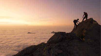 Two mountain climbers near the summit of a mountain at sunset.