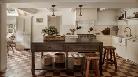 A white kitchen with a dark wood freestanding island and a beige and brown checkerboard floor