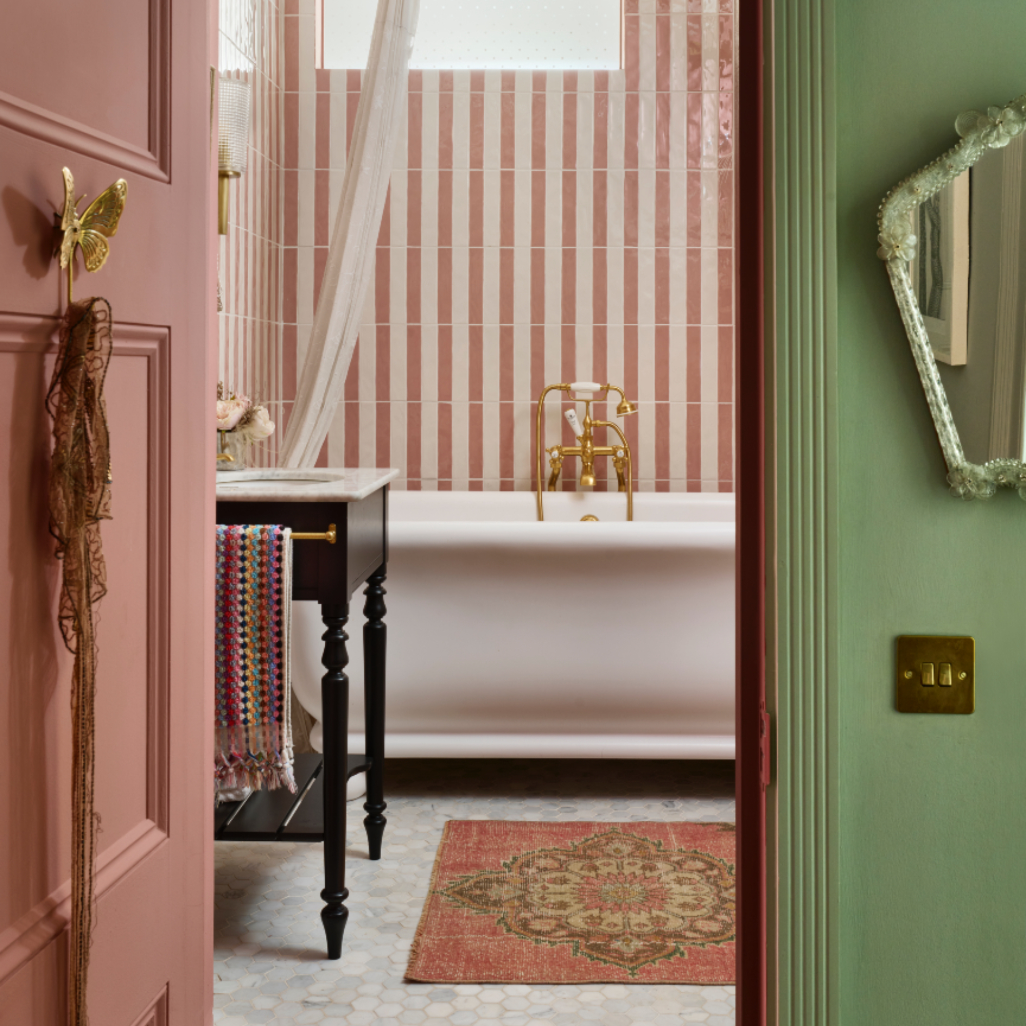 Pearl Lowe's bathroom with pink and white tiles, large classic white bath, marble floor tiles, rug, vintage washstand
