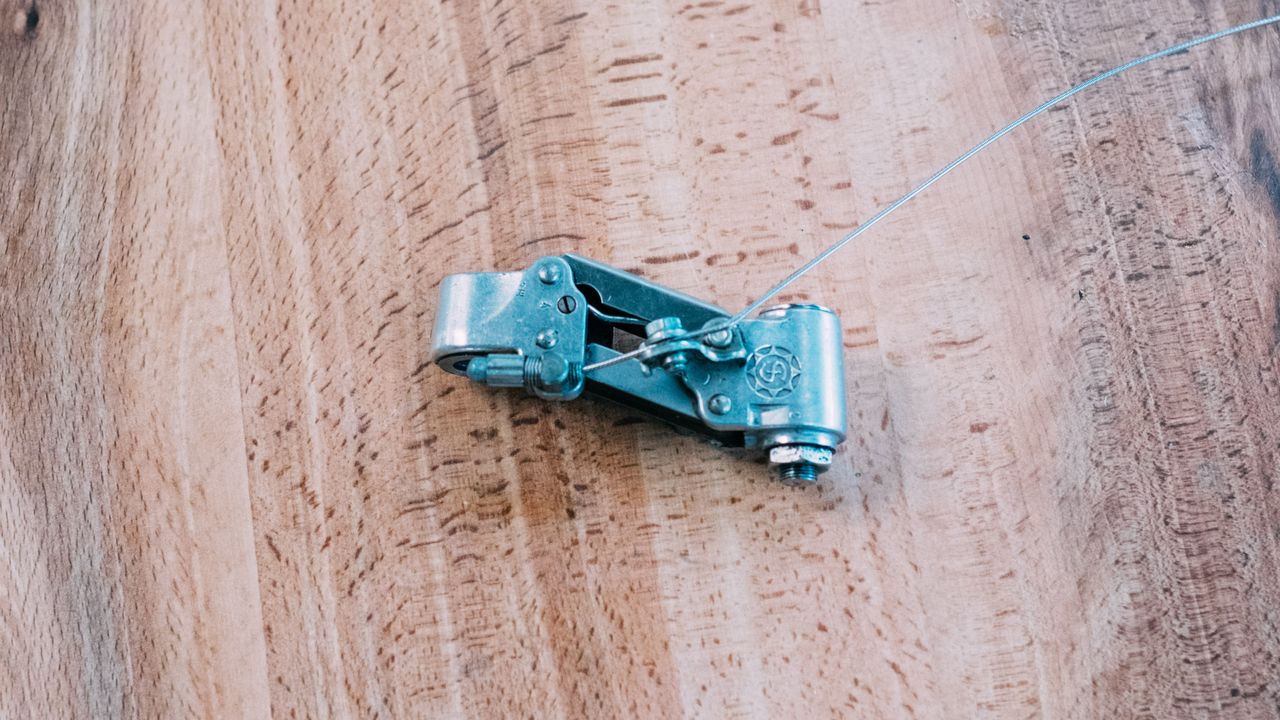 The silver body of a rear derailleur sits on a wooden table