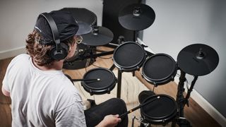 Man wearing headphones plays an Alesis Nitro Mesh drum set