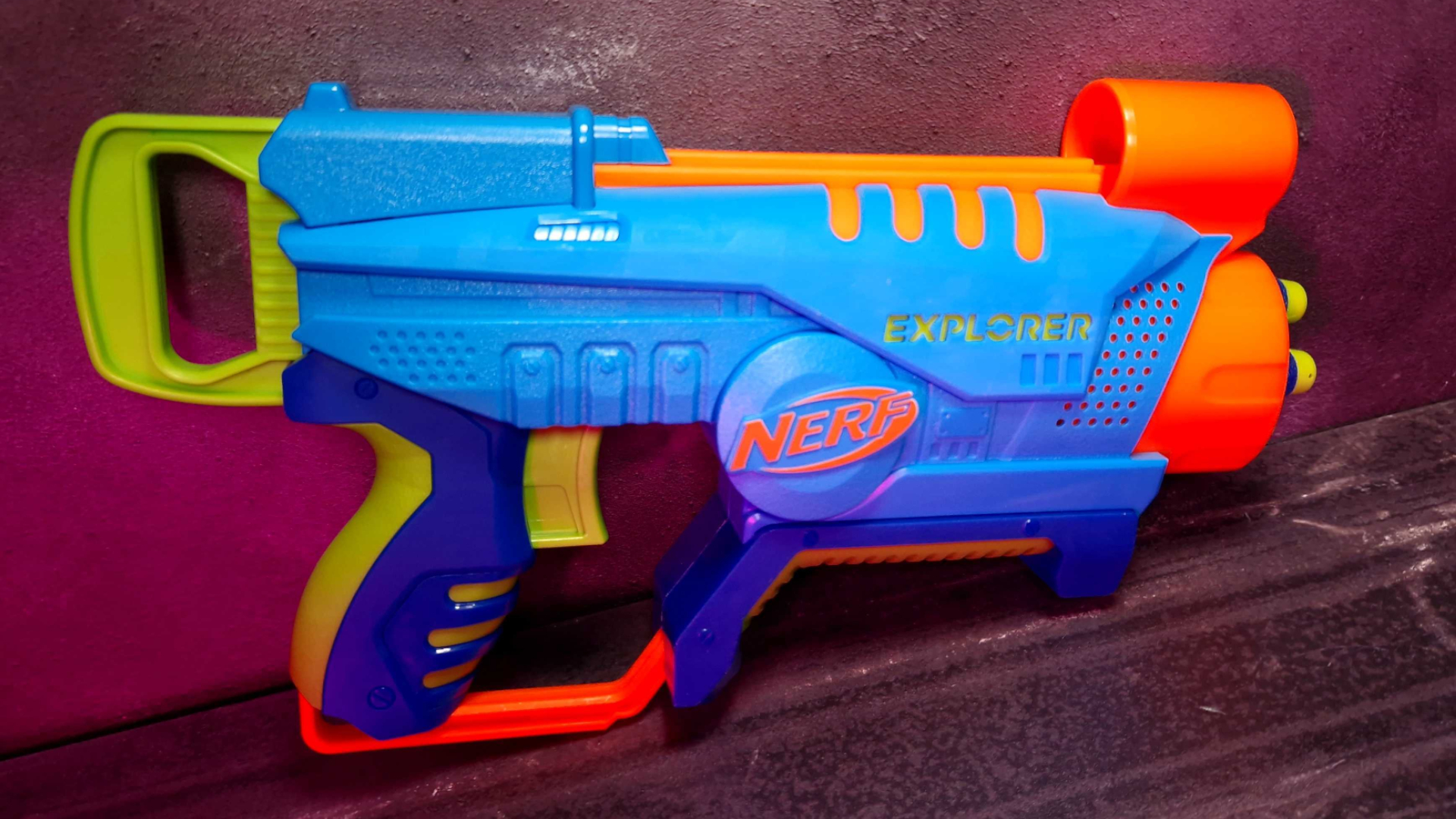 Un lanzador Nerf Elite Jr. Explorer, apoyado contra un fondo oscuro