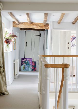 landing at top of staircase with beamed ceiling with wooden doorframes and artwork