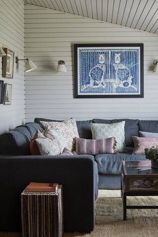 Blue corner sofa in a white room with wood clad walls and blue paintings
