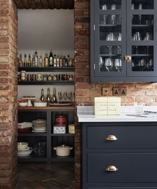 Kitchen with doorway to pantry storage, an exposed brick wall and blue grey painted cupboard and shelves.