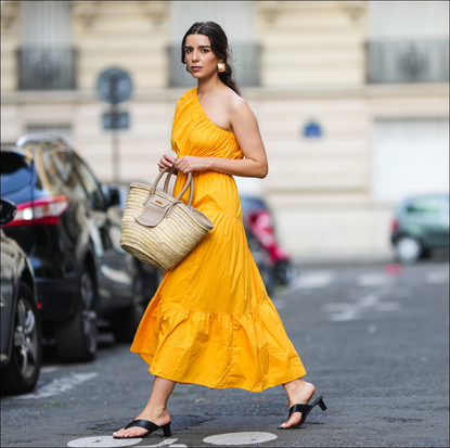 Ketevan Giorgadze @katie.one wears a one shoulder cut out maxi dress in orange from Mango, oversized golden hoop earrings from Zara, flip flop heeled black sandals shoes from APC Paris, a Le Grand Panier beach straw bag by Jacquemus, on August 12, 2021 in Paris, France. (Photo by Edward Berthelot/Getty Images)