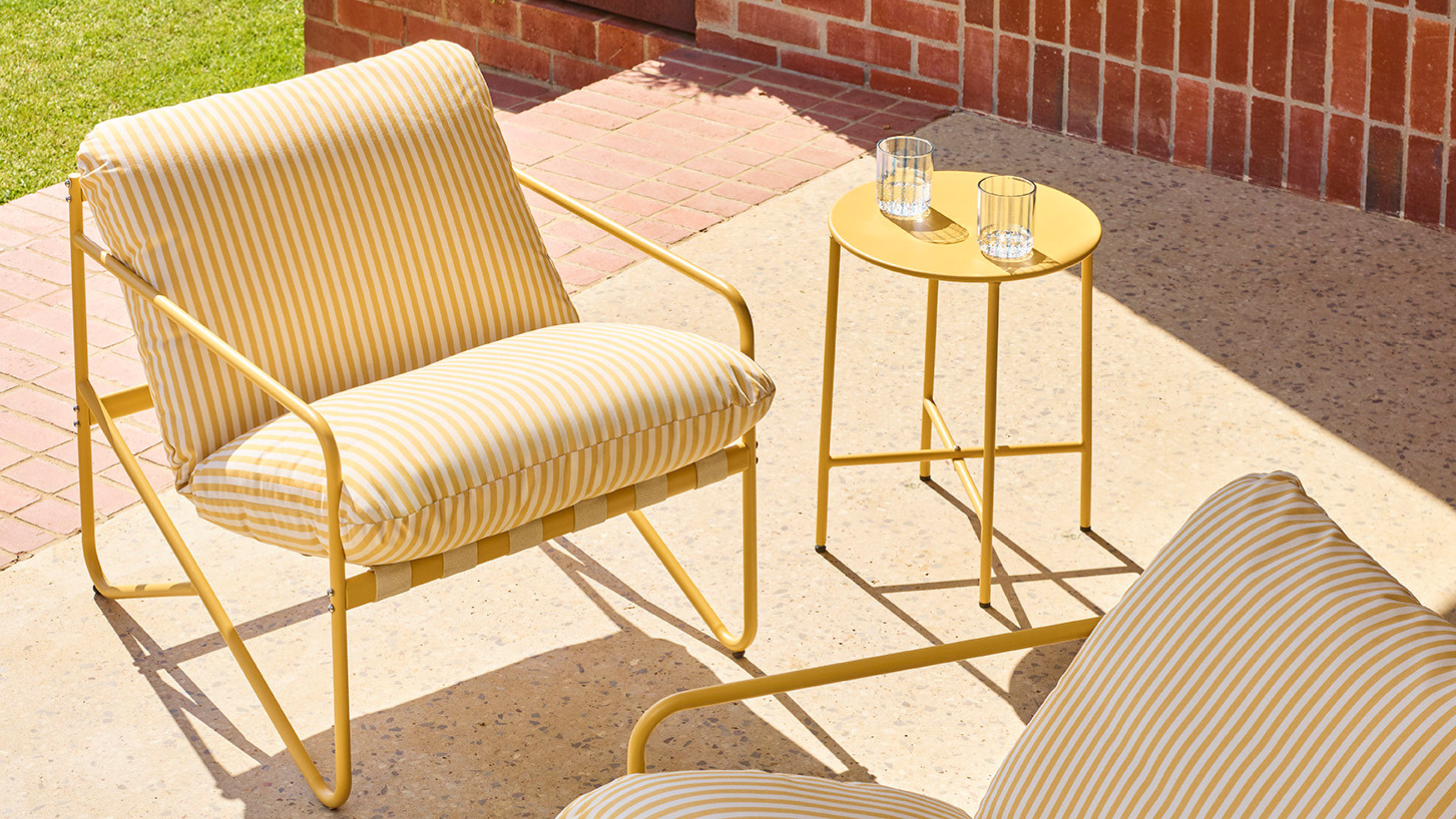 Yellow Tuscany Bistro Set positioned on a sunny patio. One chair and the coffee table is in full view. The second chair is partially in focus.