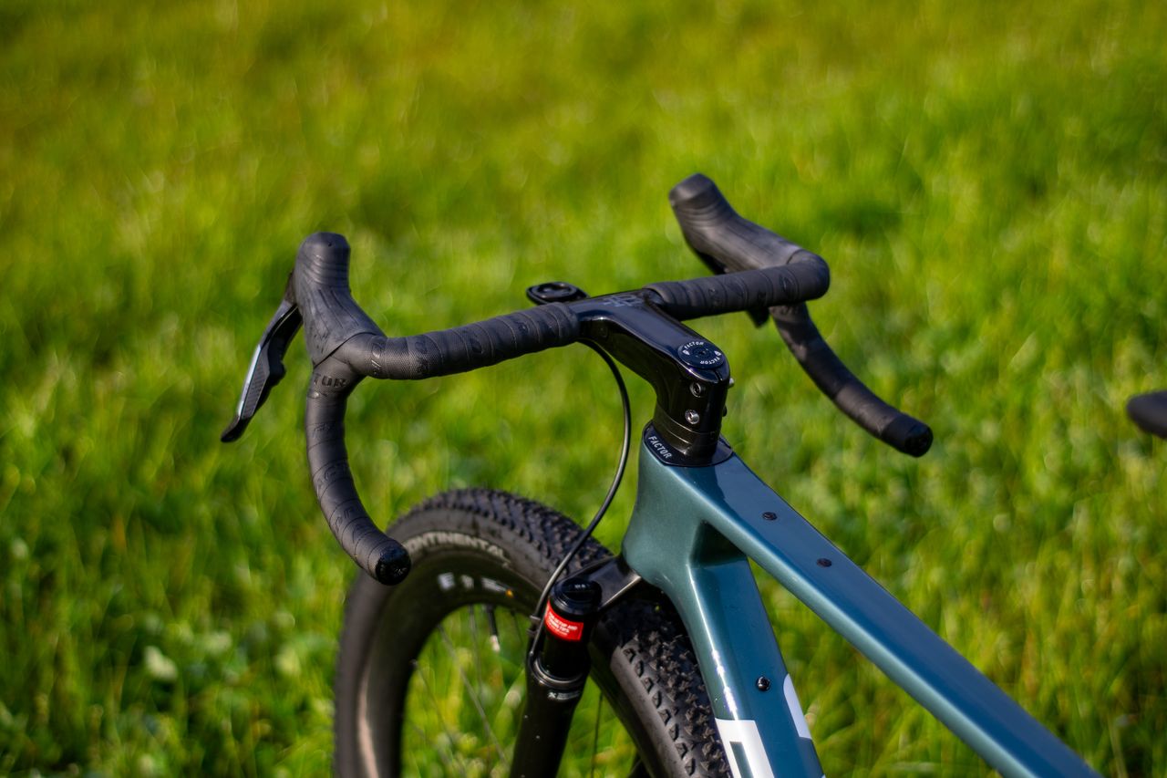 A blue Factor Sarana gravel bike in a grassy field with a hedge in the background
