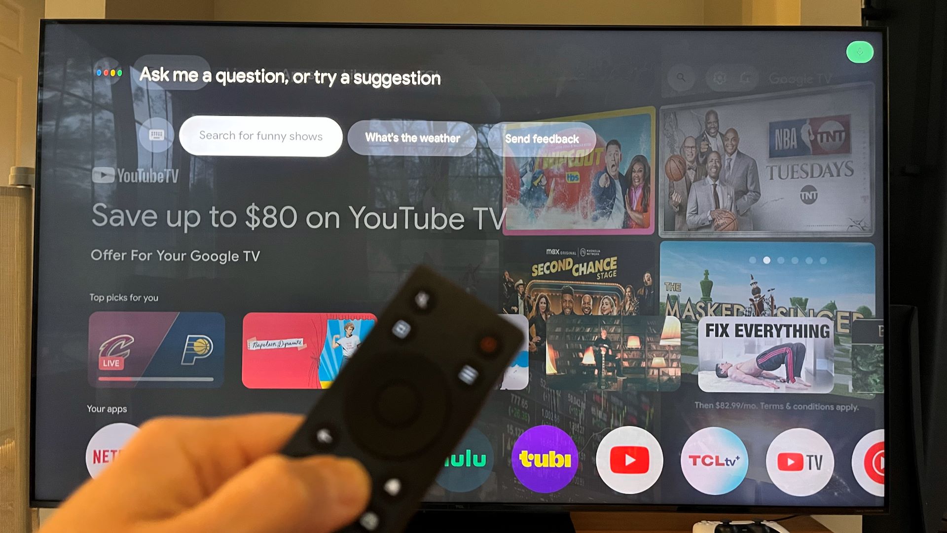 TCL QM7K Google TV home screen with hand holding remote in front