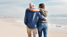 A male and female couple walks on the beach.