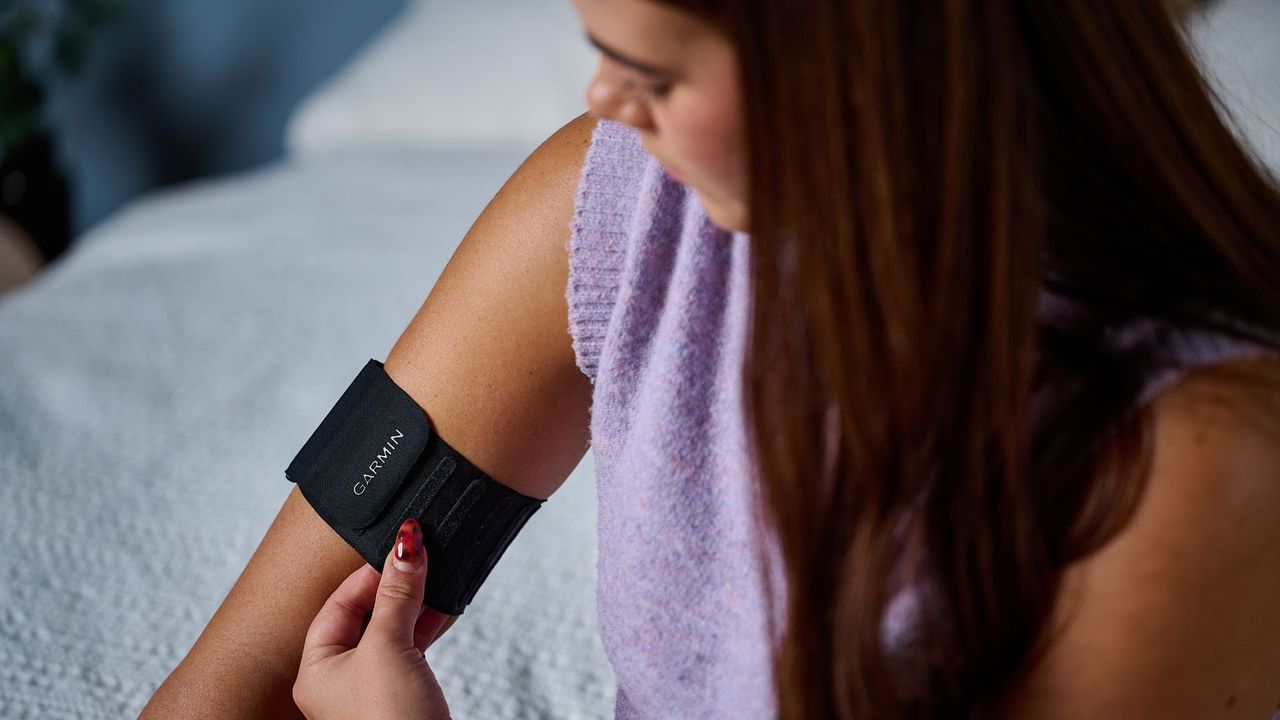 Tom's Guide's sleep tech tester wearing a purple top placing the Garmin Index Sleep Monitor on right upper arm