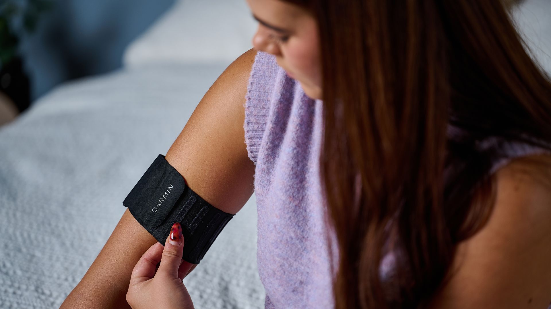 Tom's Guide's sleep tech tester wearing a purple top placing the Garmin Index Sleep Monitor on right upper arm 