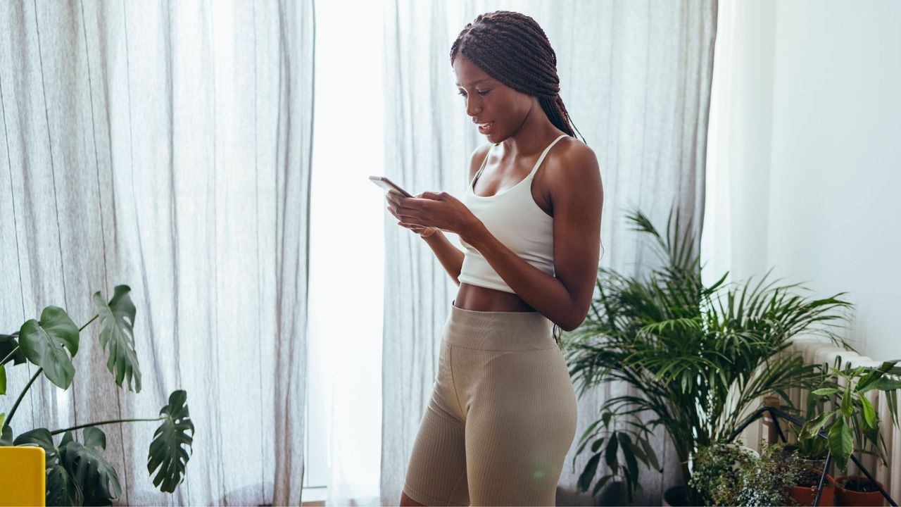 prime day pilates deals - woman in pilates clothes looking at her phone - getty images 1333812705