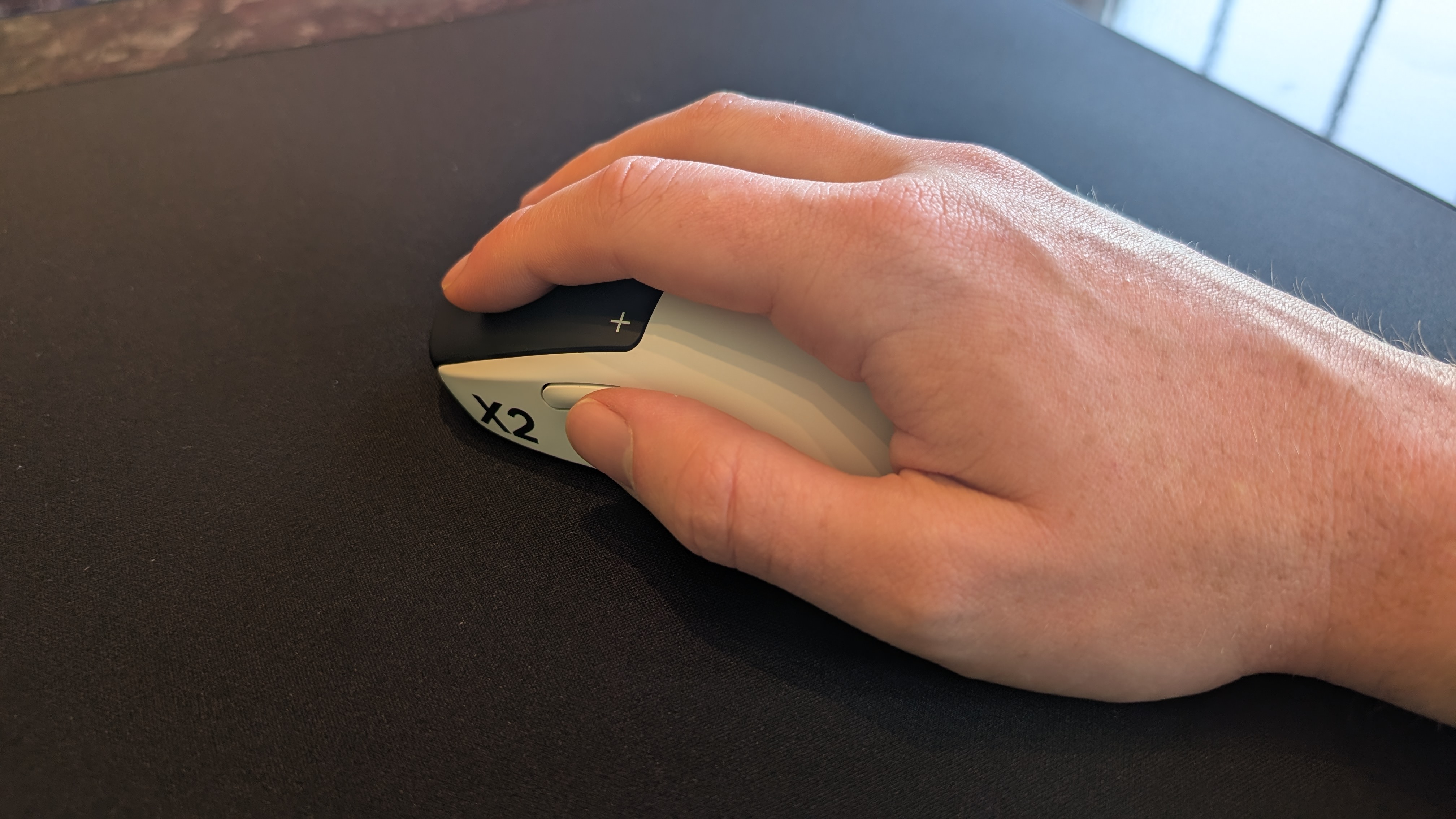 The Logitech G Pro X2 Superstrike pictured on a black mouse mat with a male hand holding it in a palm-style grip.