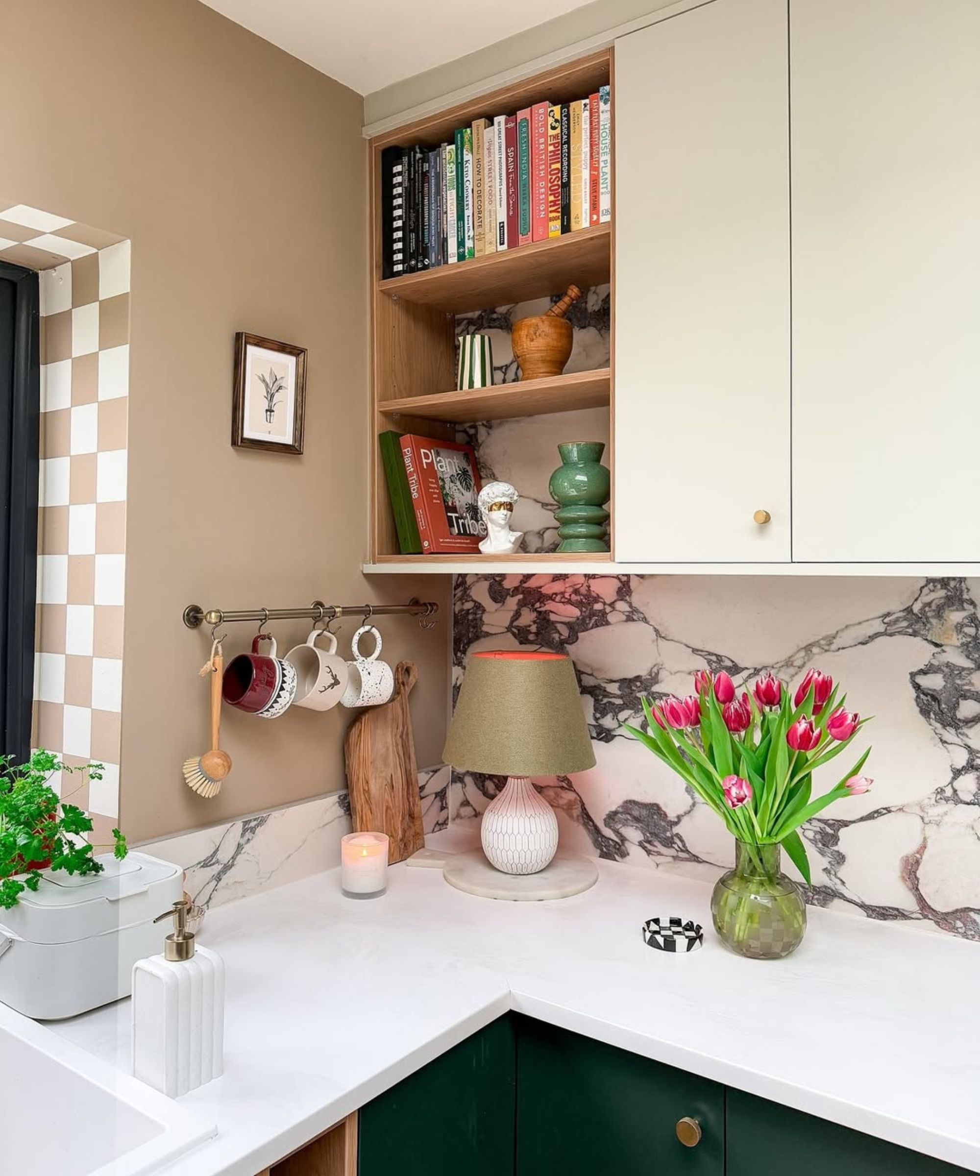 kitchen with marble backsplash, dark green cabinets and cream cabinets, bookshelf, pot rail with mugs hanging and taupe wall with checkered border