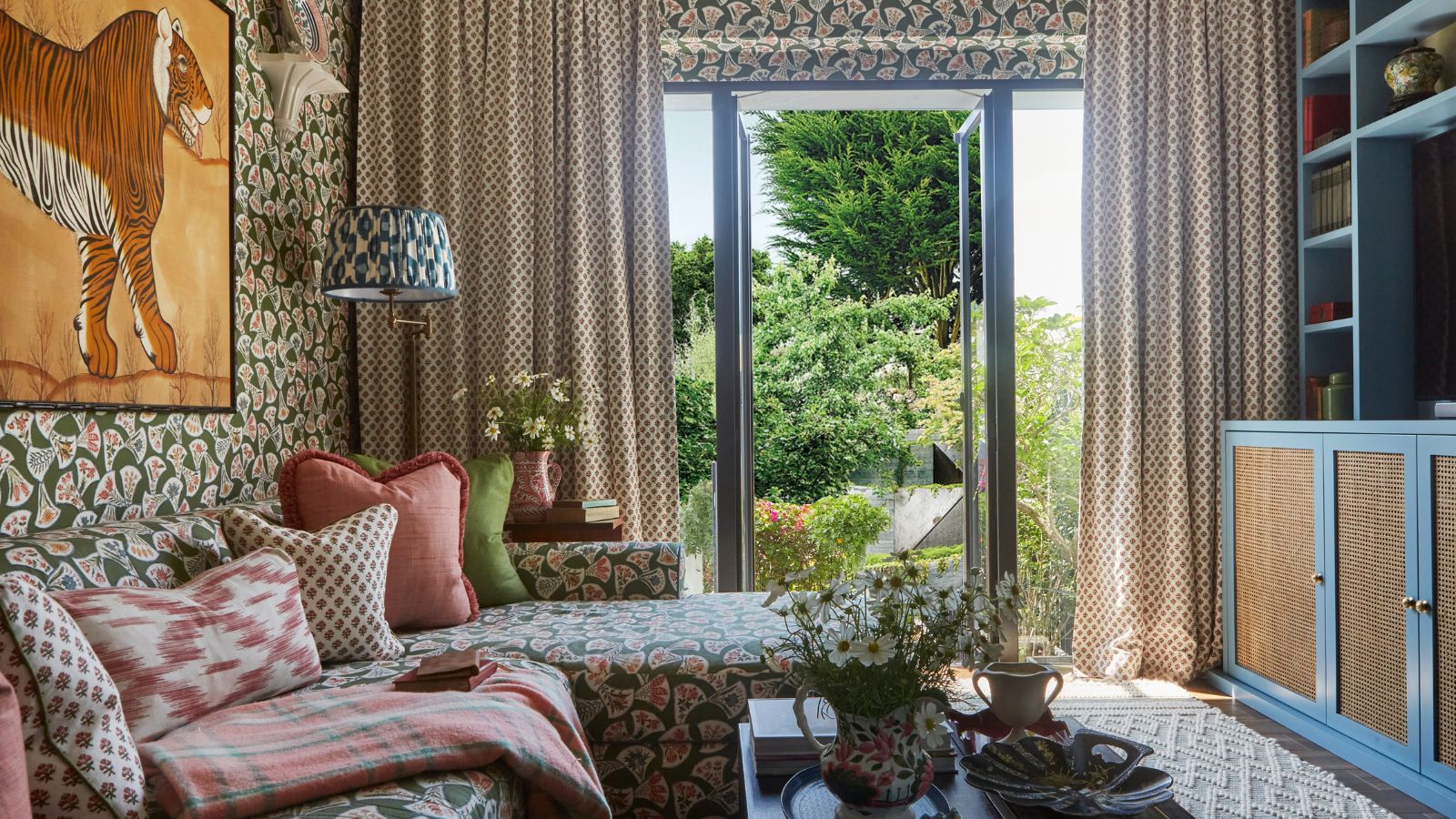 a pattern drenched living room in London by designer Elizabeth Hay with patio doors onto the garden and a blue media wall