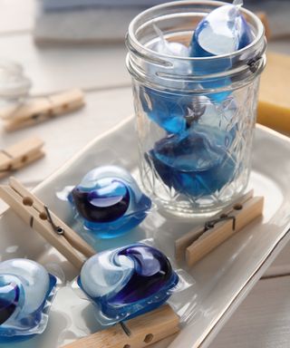 A selection of blue laundry capsule pods in a glass jar with wooden pegs