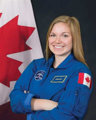 Canadian Space Agency astronaut Jenni Sidey-Gibbons standing in front of the canadian flag in a blue flight suit