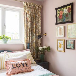 A pink-painted bedroom with a cluster of small artworks hung on the side wall