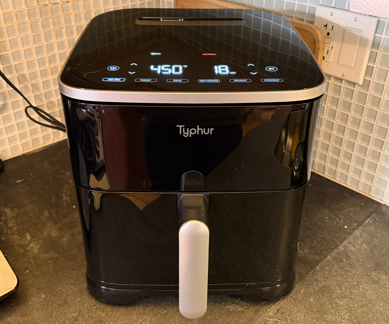 A black Typhur Sync air fryer on a grey kitchen counter against a blue micro-tile backsplash