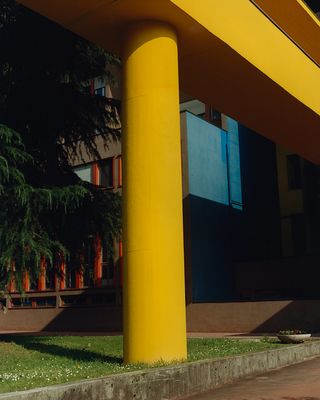 A yellow pillar on grass supporting a raised yellow wallkway connecting blocks to each other