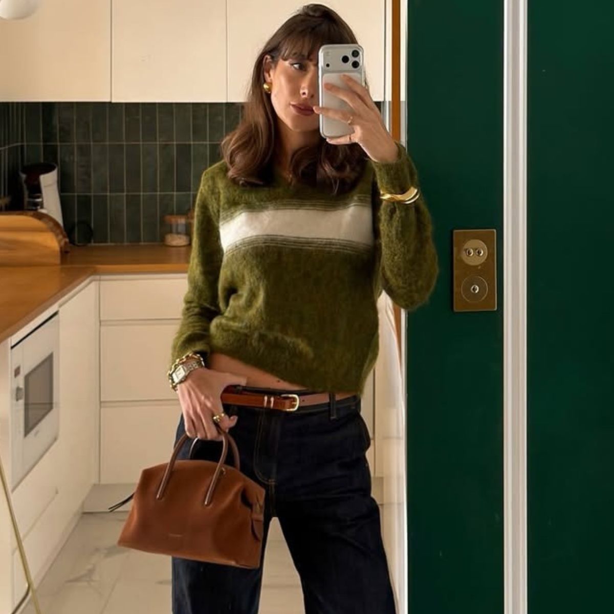 Woman wears green and white striped jumper, blue jeans and carries small suede bag
