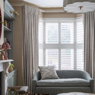 Living room with grey sofa and large full-length curtains over sash windows.