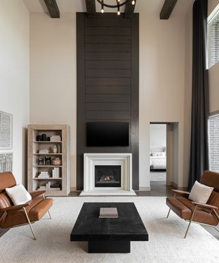 Neutral living room with double height ceiling, leather armchairs, coffee table, area rug and fireplace