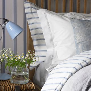 bedroom with multicolour wall and bedding with cushion and duvet and bedside blue lamp and glass jar with flower