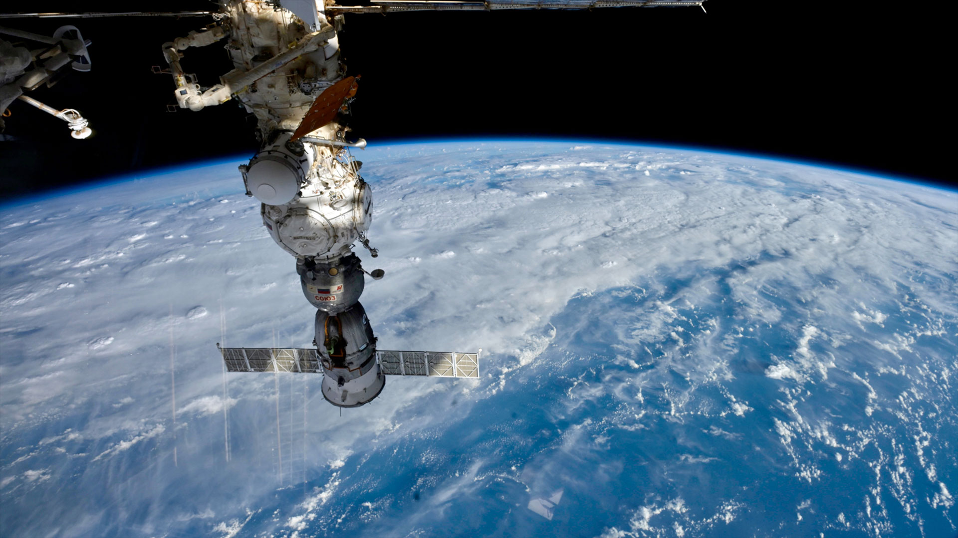 a spacecraft and space station modules are seen docked together above the blue and white Earth below.