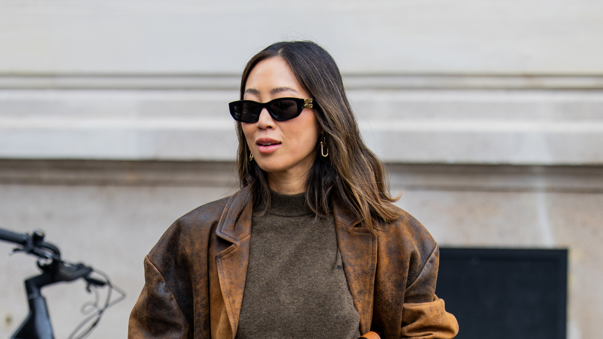 Aimee Song wears brown jumper, leather jacket, grey pants, brown bag outside Miu Miu during the Womenswear Spring Summer 2026 as part of Paris Fashion Week on October 06, 2025 in Paris, France