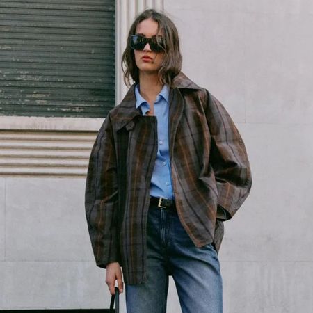 Woman wears check trench coat, blue shirt, blue jeans and black belt